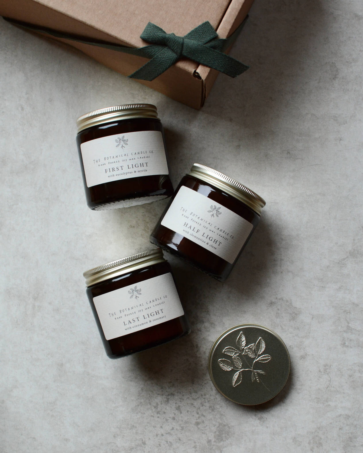 Three glass candles, next to a gift box with green ribbon.