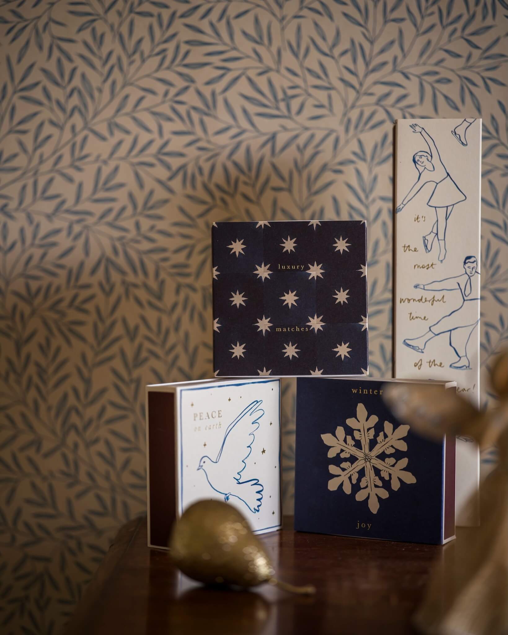 Decorative matchboxes with artistic designs, shown against a patterned wall background.