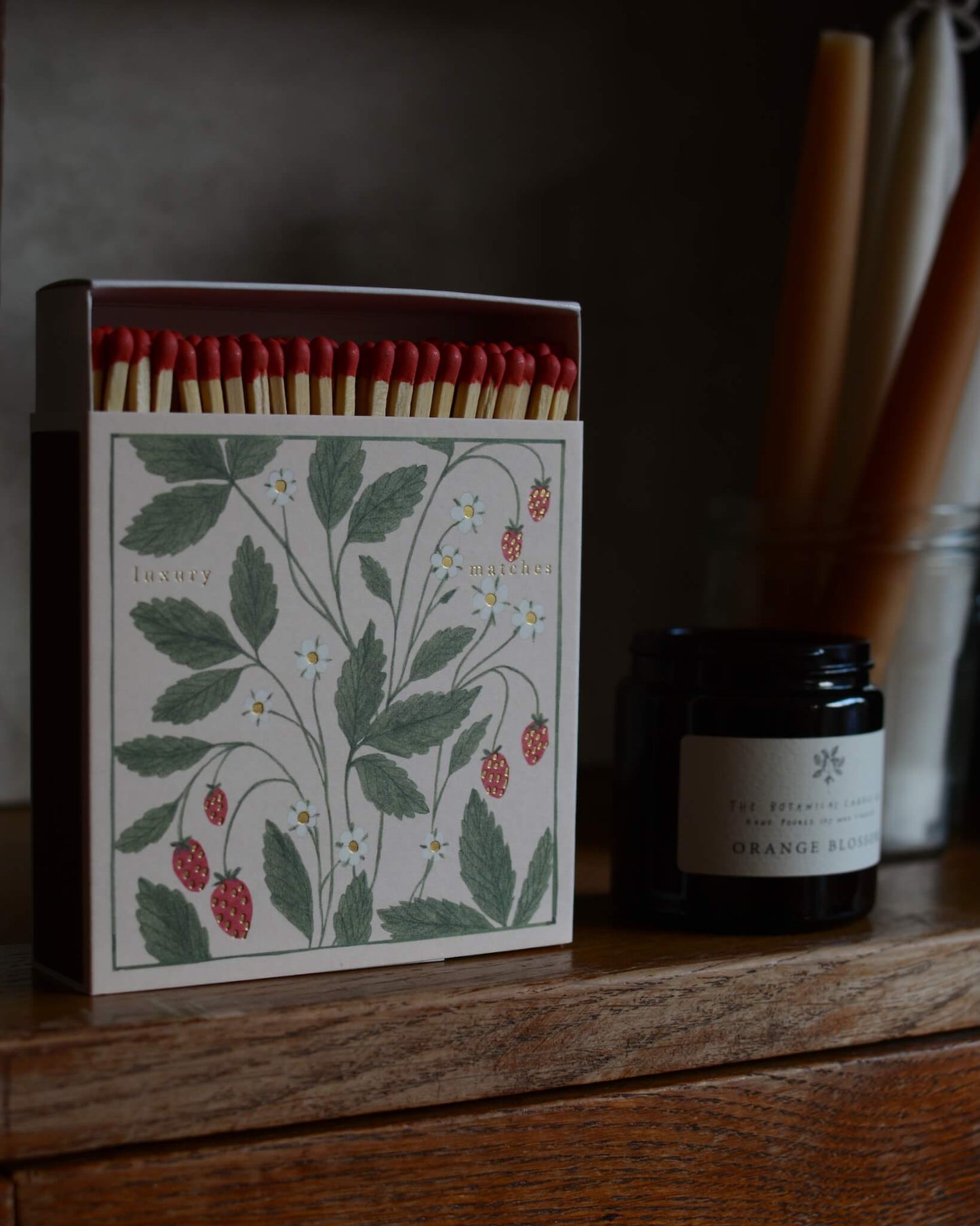 Close-up of a matchbox featuring an illustration of wild strawberries, with gold leaf detailing.