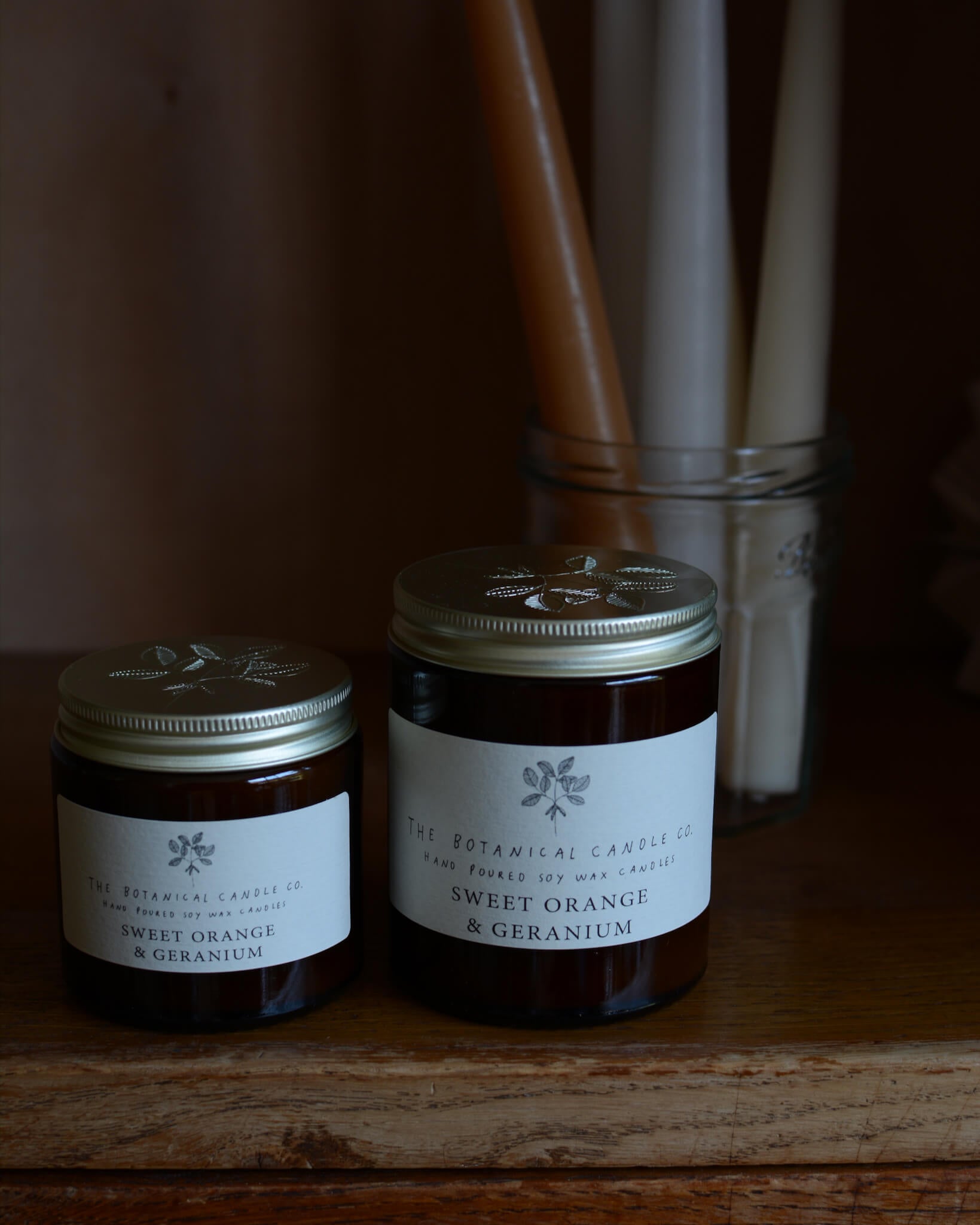 Sweet Orange and Geranium soy wax candle by The Botanical Candle Co. next to beeswax candles.