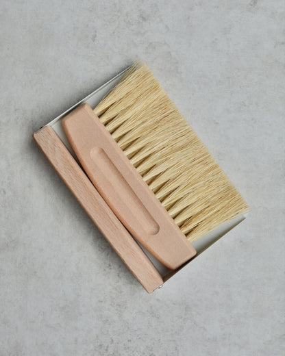 Wooden and metal dustpan and brush set on a grey background.