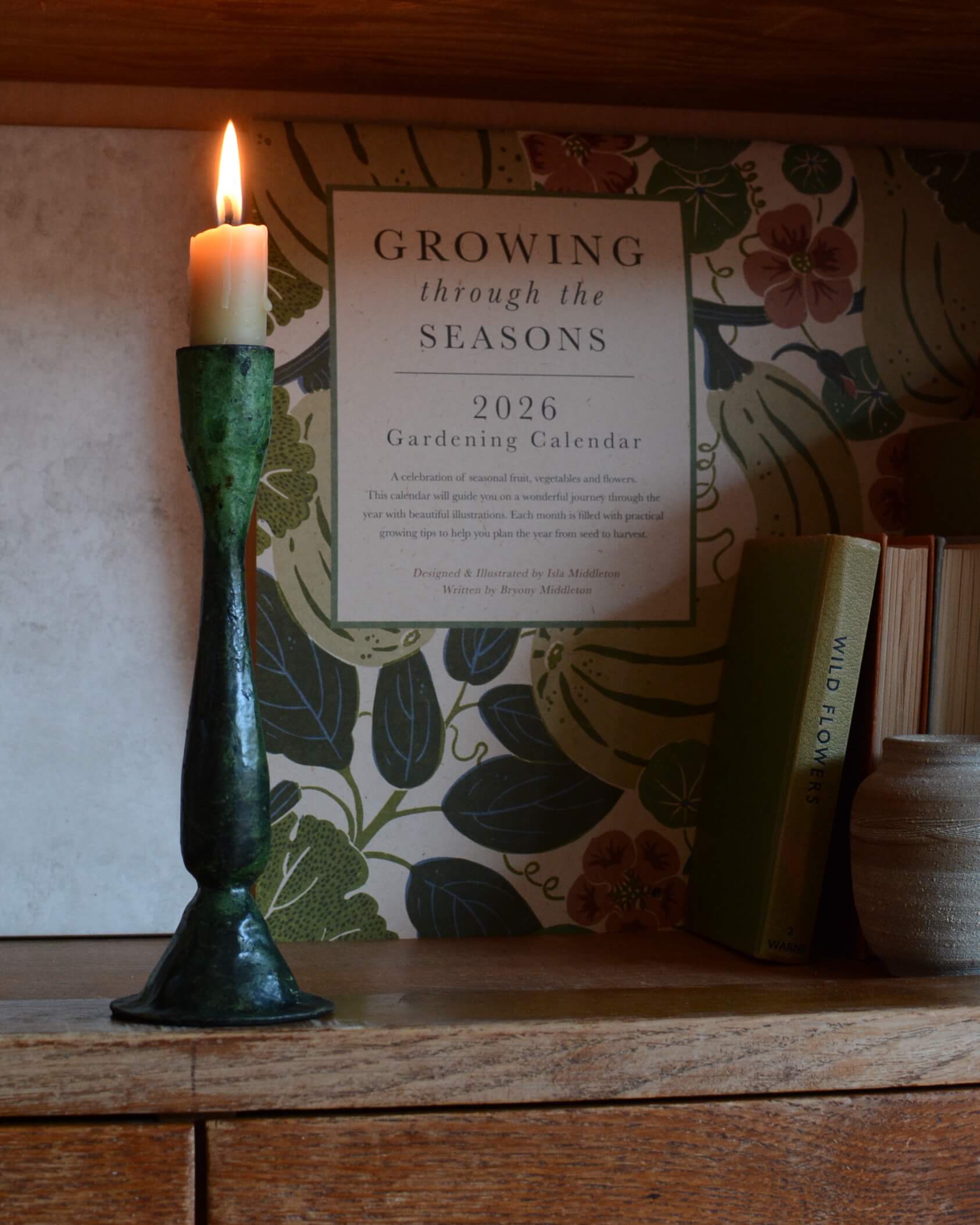 A green verdigris tall candle holder, for dinner candles, shown with a lit beeswax candle.