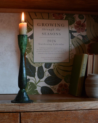 A green verdigris tall candle holder, for dinner candles, shown with a lit beeswax candle.