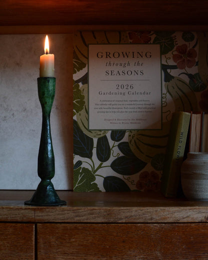 A green verdigris tall candle holder, for dinner candles, shown with a lit beeswax candle.