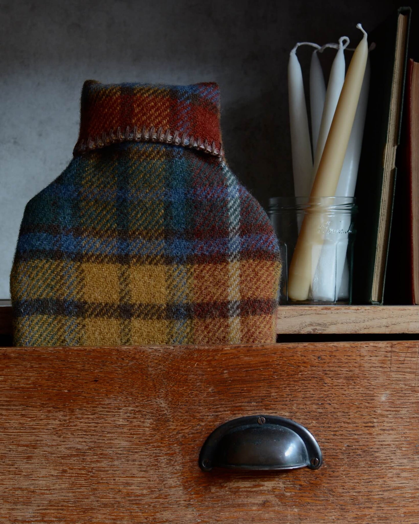 Plaid wool hot water bottle on a wooden surface with candles in the background