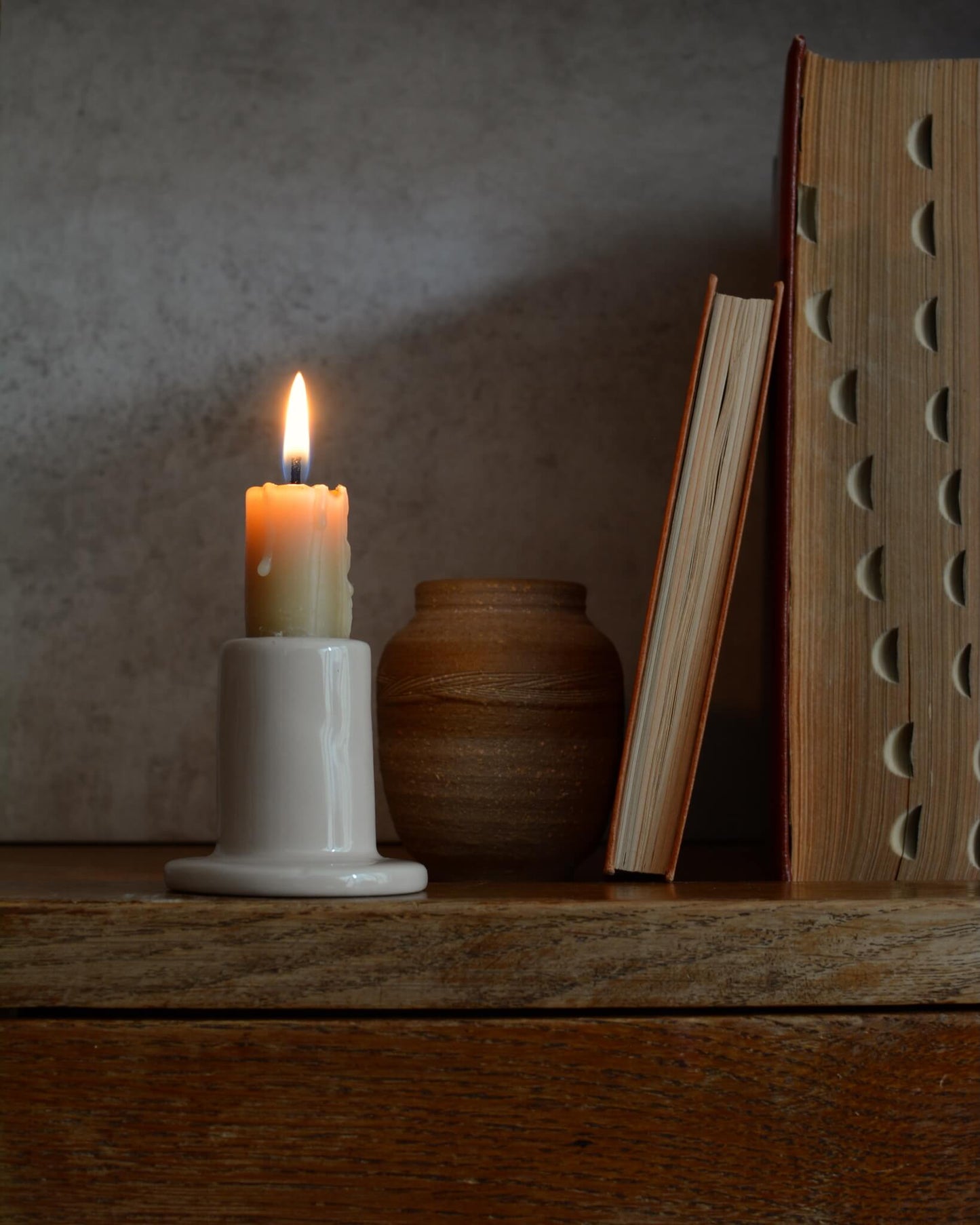 A beeswax candle in a cream holder on a wooden surface with a textured wall background
