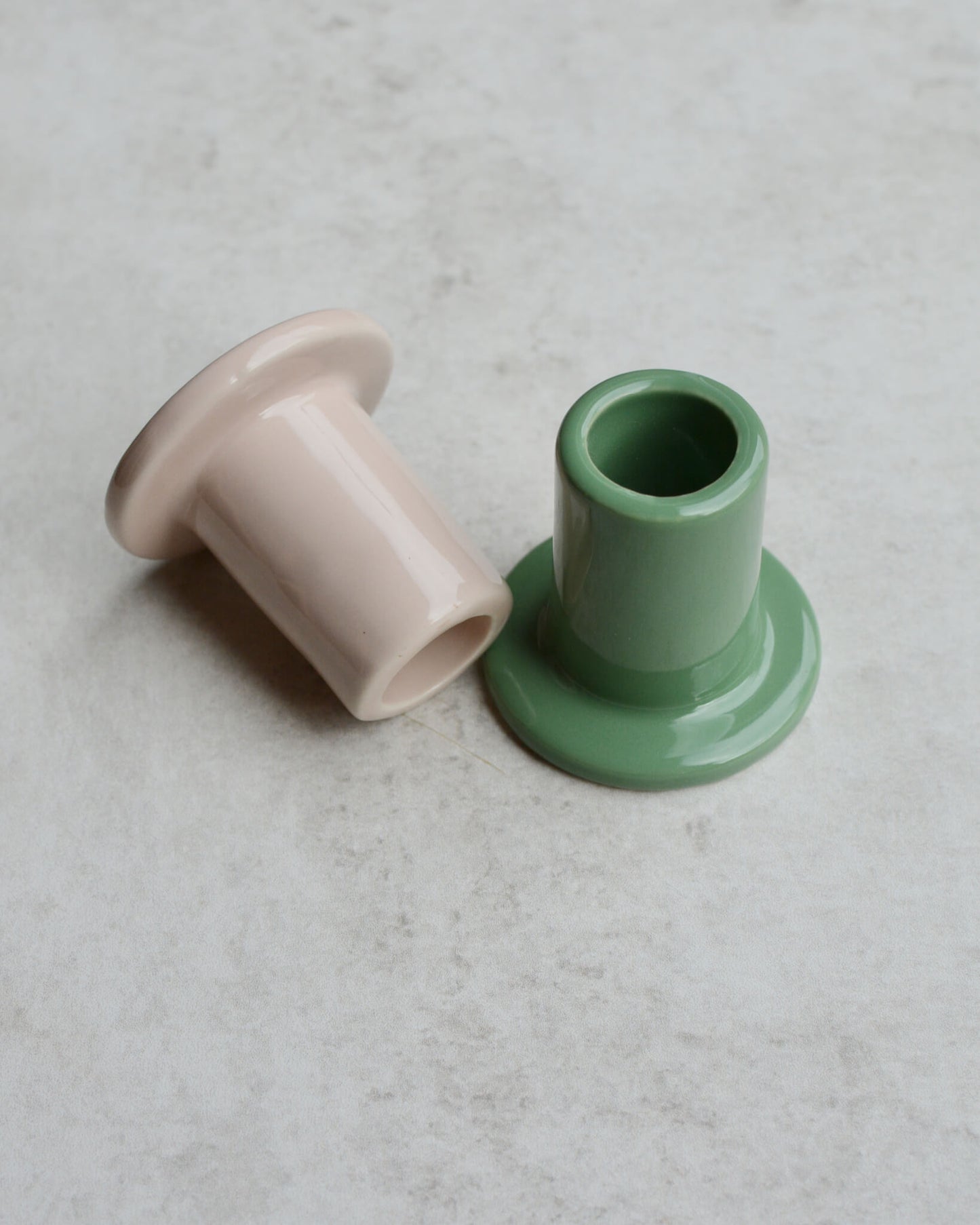 Two ceramic candle holders, one taupe and one green, on a light grey surface.