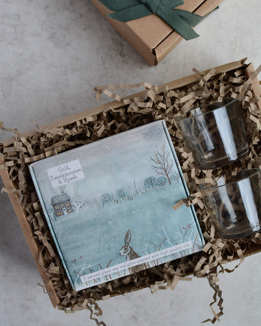 Gift set with a box of tealights and a pair of glass votives, in a box on a grey surface.