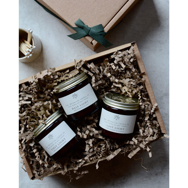 Gift box containing 3 amber glass jar candles with silver lids.