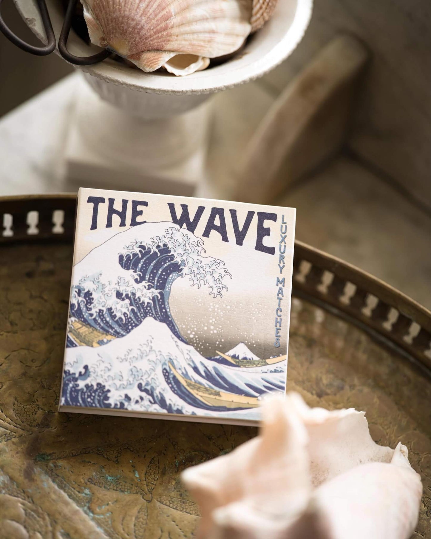 Box of matches titled 'The Wave' with a wave design on a bathroom surface with shells.