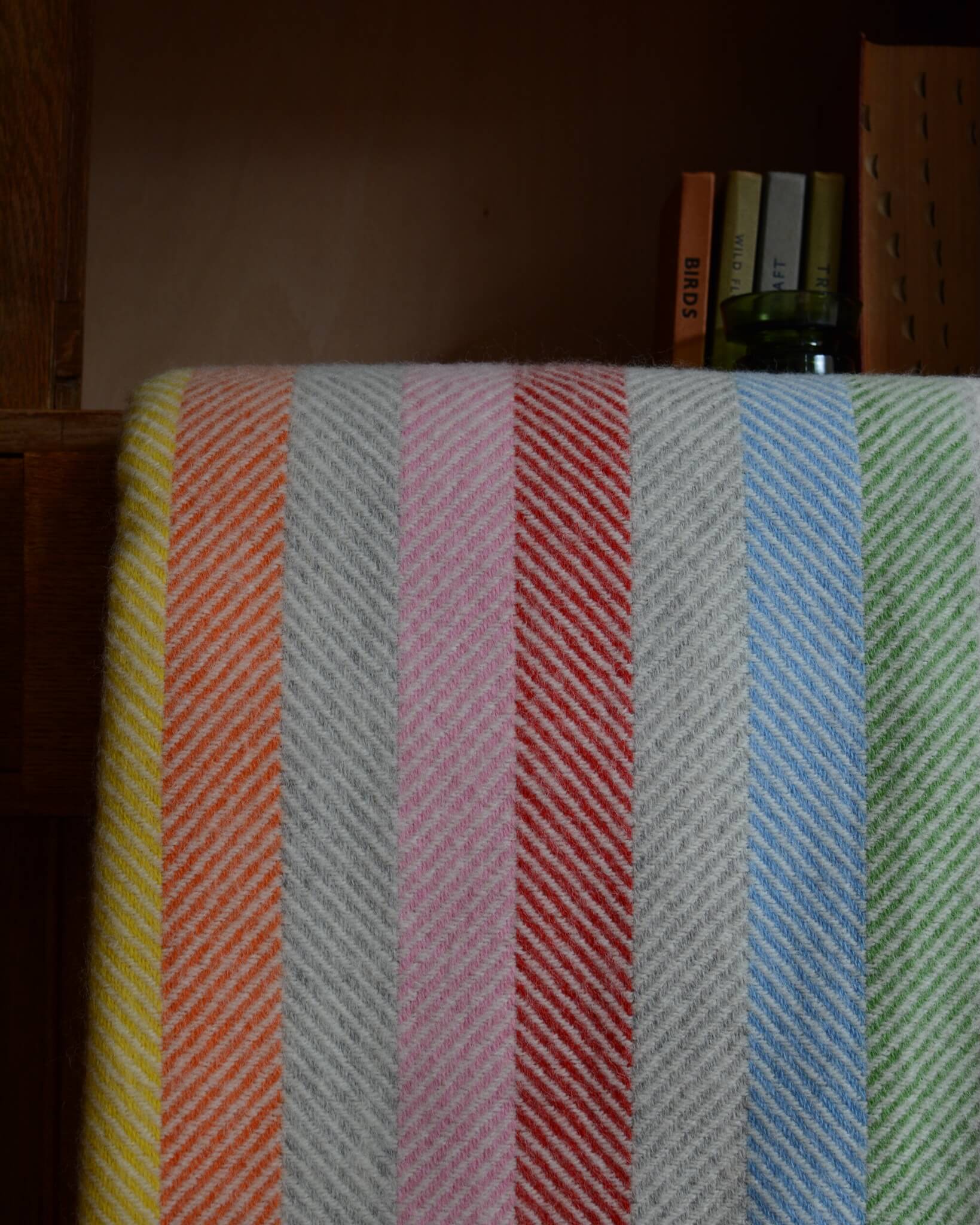 Close up of a colourful rainbow striped wool blanket with books shown behind.