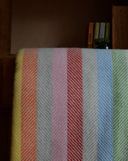 Close up of a colourful rainbow striped wool blanket with books shown behind.