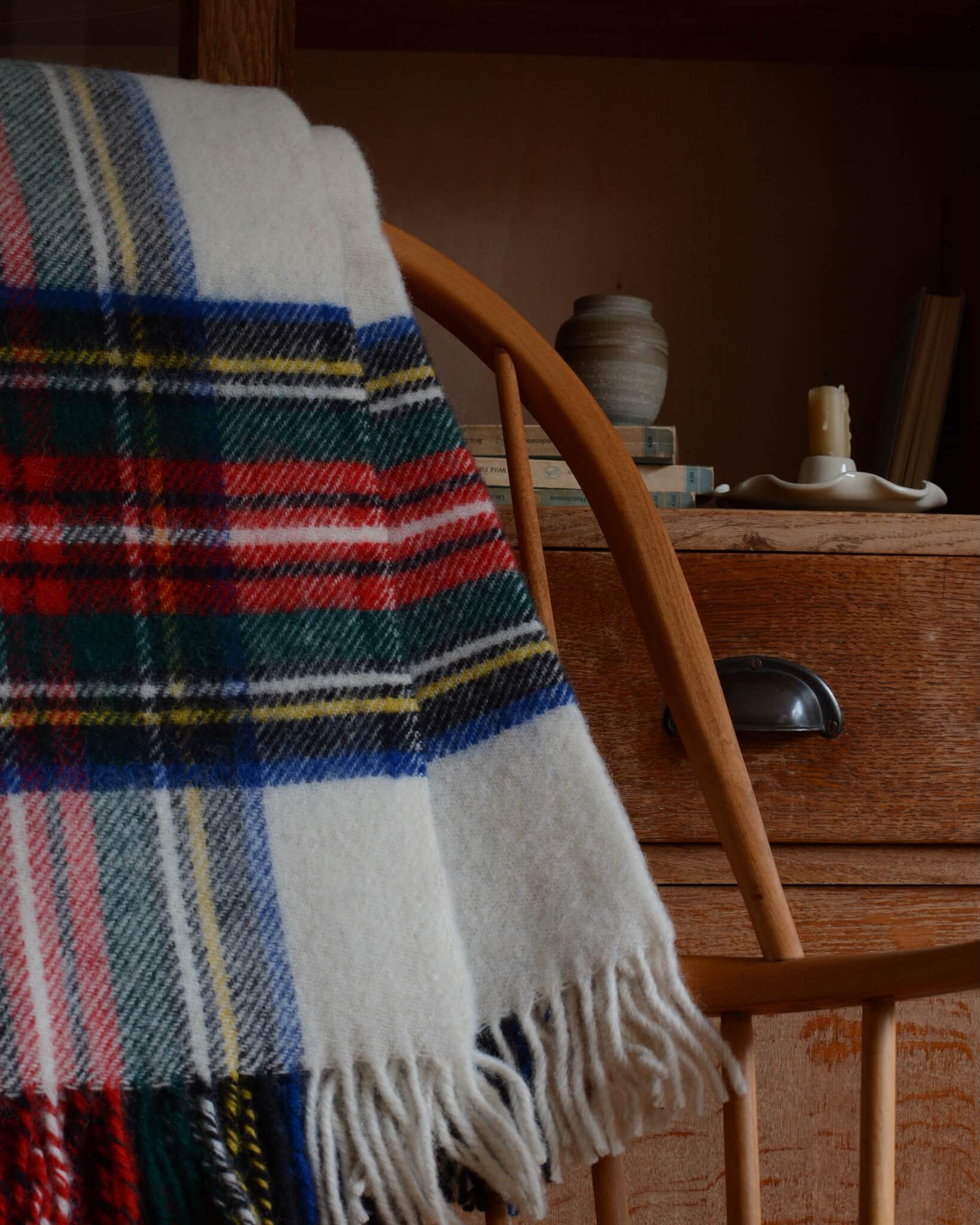 Close up of a plaid wool blanket with colourful pattern, shown on a wooden rocking chair.