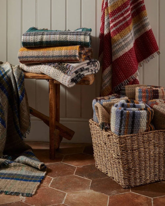 Stack of colourful recycled wool blankets on a wooden stool and in a woven basket against a wooden panelled wall.