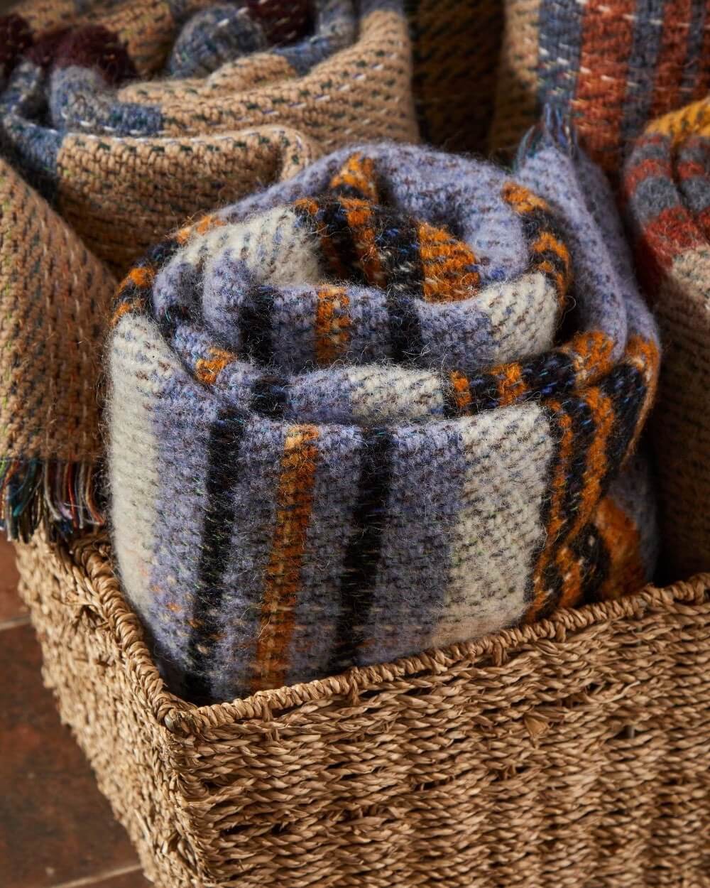 Folded recycled wool blanket in a woven basket with other blankets in the background