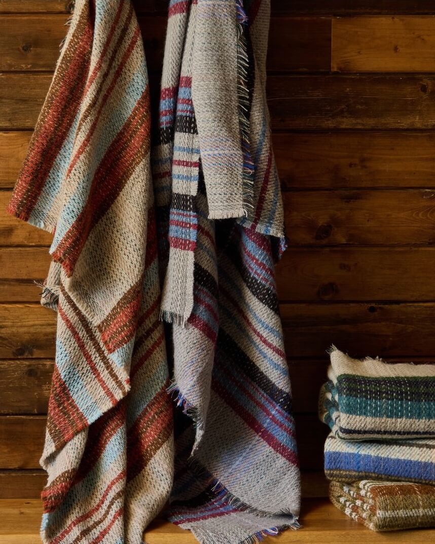 Recycled wool blankets with colourful stripes draped over a wooden surface.