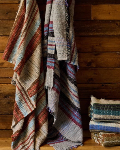 Recycled wool blankets with colourful stripes draped over a wooden surface.