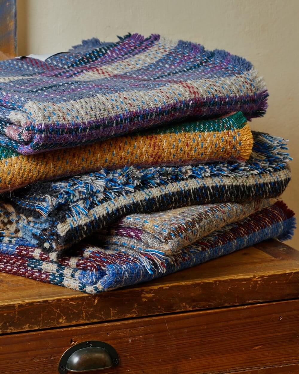 Stack of colorful woven blankets on a wooden surface