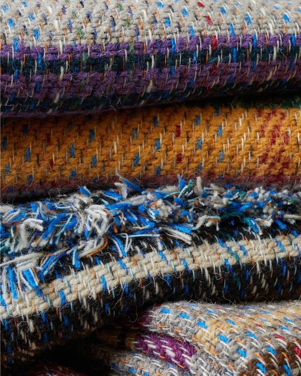 Stack of textured recycled wool blankets with different patterns and colours.