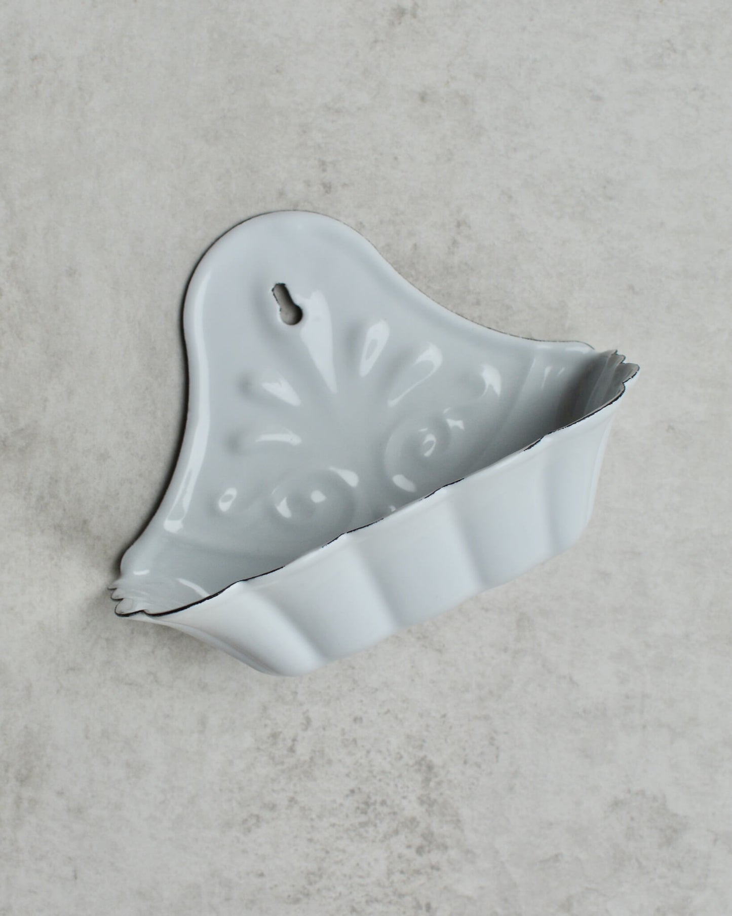 Vintage-style white enamel wall-mounted soap dish, with floral pattern, on a grey background.