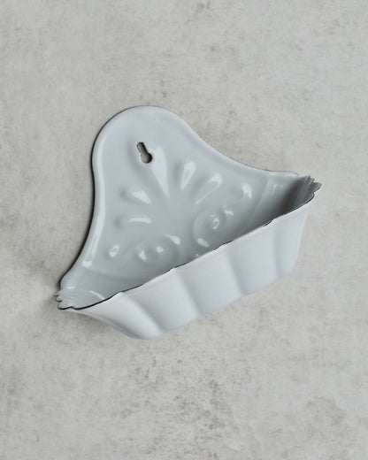 Vintage-style white enamel wall-mounted soap dish, with floral pattern, on a grey background.
