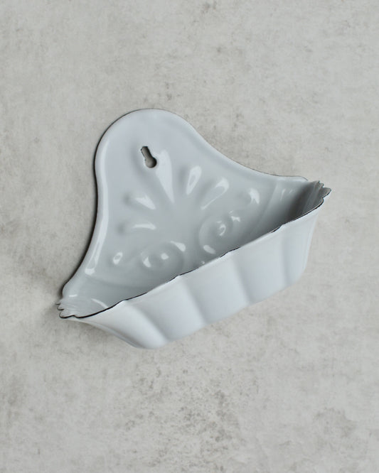 Vintage-style white enamel wall-mounted soap dish, with floral pattern, on a grey background.