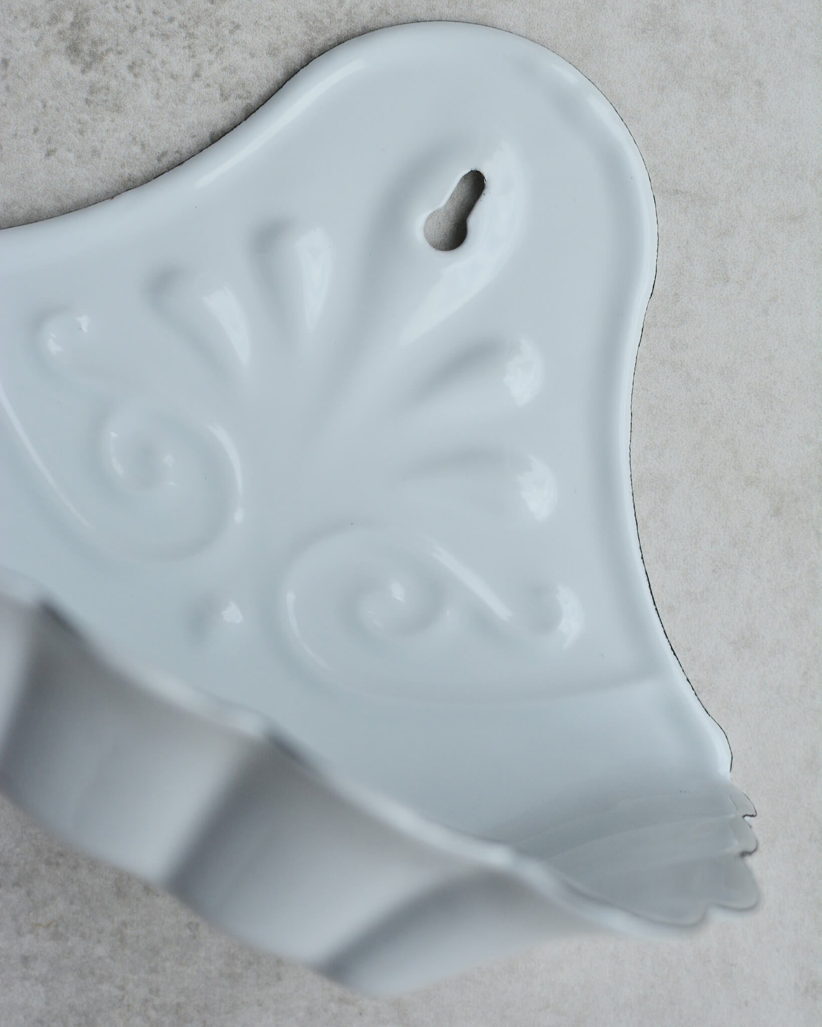 Vintage-style white enamel wall-mounted soap dish, with floral pattern, on a grey background.