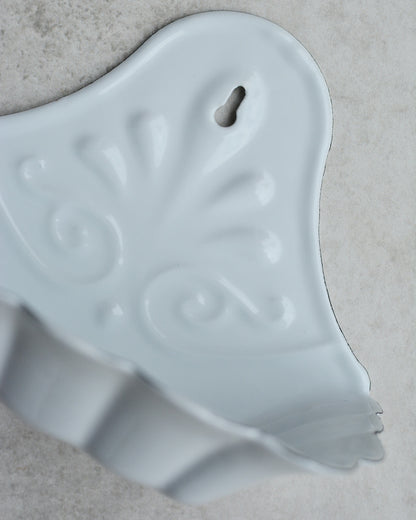 Vintage-style white enamel wall-mounted soap dish, with floral pattern, on a grey background.