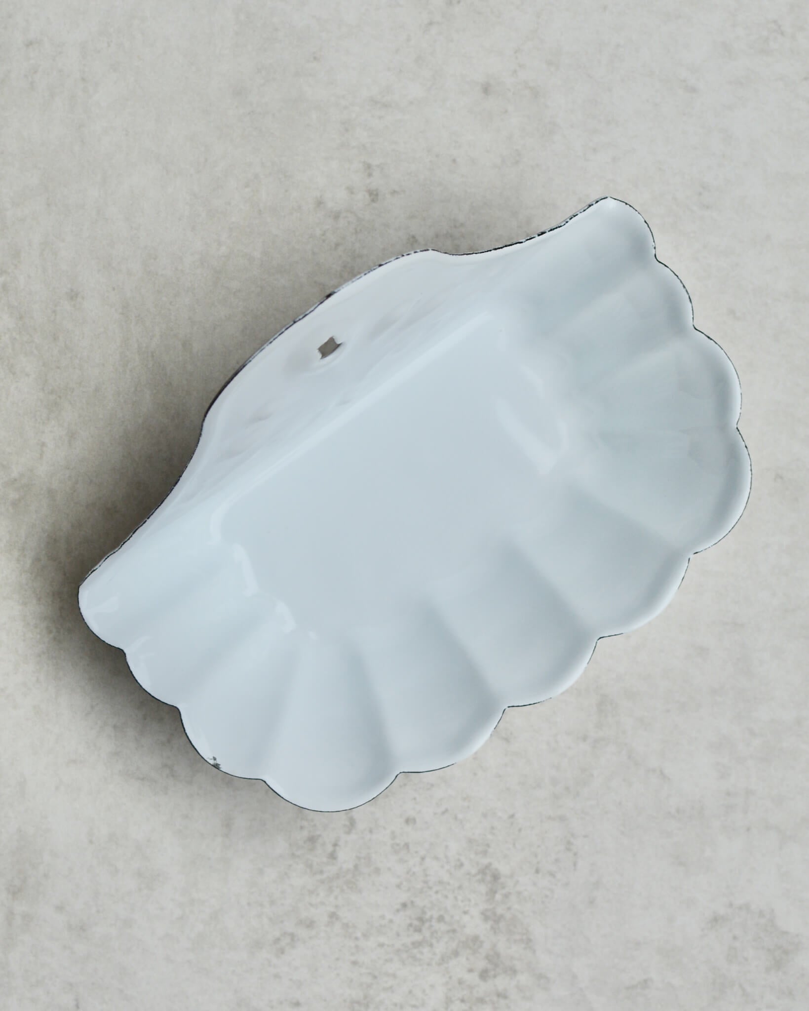 Vintage-style white enamel wall-mounted soap dish, with floral pattern, on a grey background.