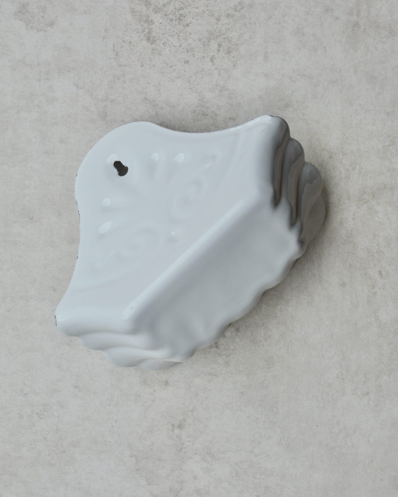 Vintage-style white enamel wall-mounted soap dish, with floral pattern, on a grey background.