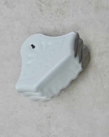 Vintage-style white enamel wall-mounted soap dish, with floral pattern, on a grey background.