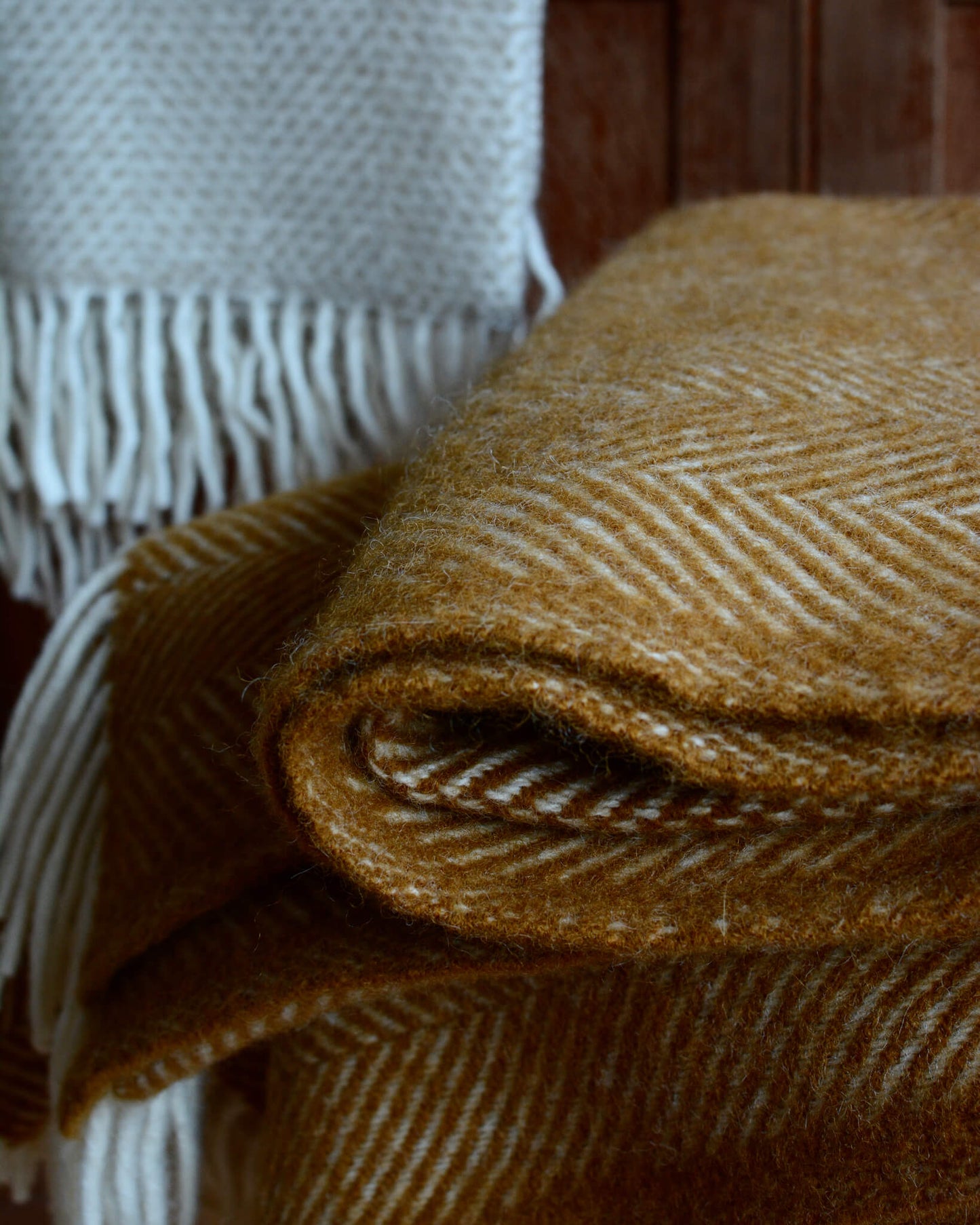 Detail of a folded mustard yellow wool herringbone blanket.