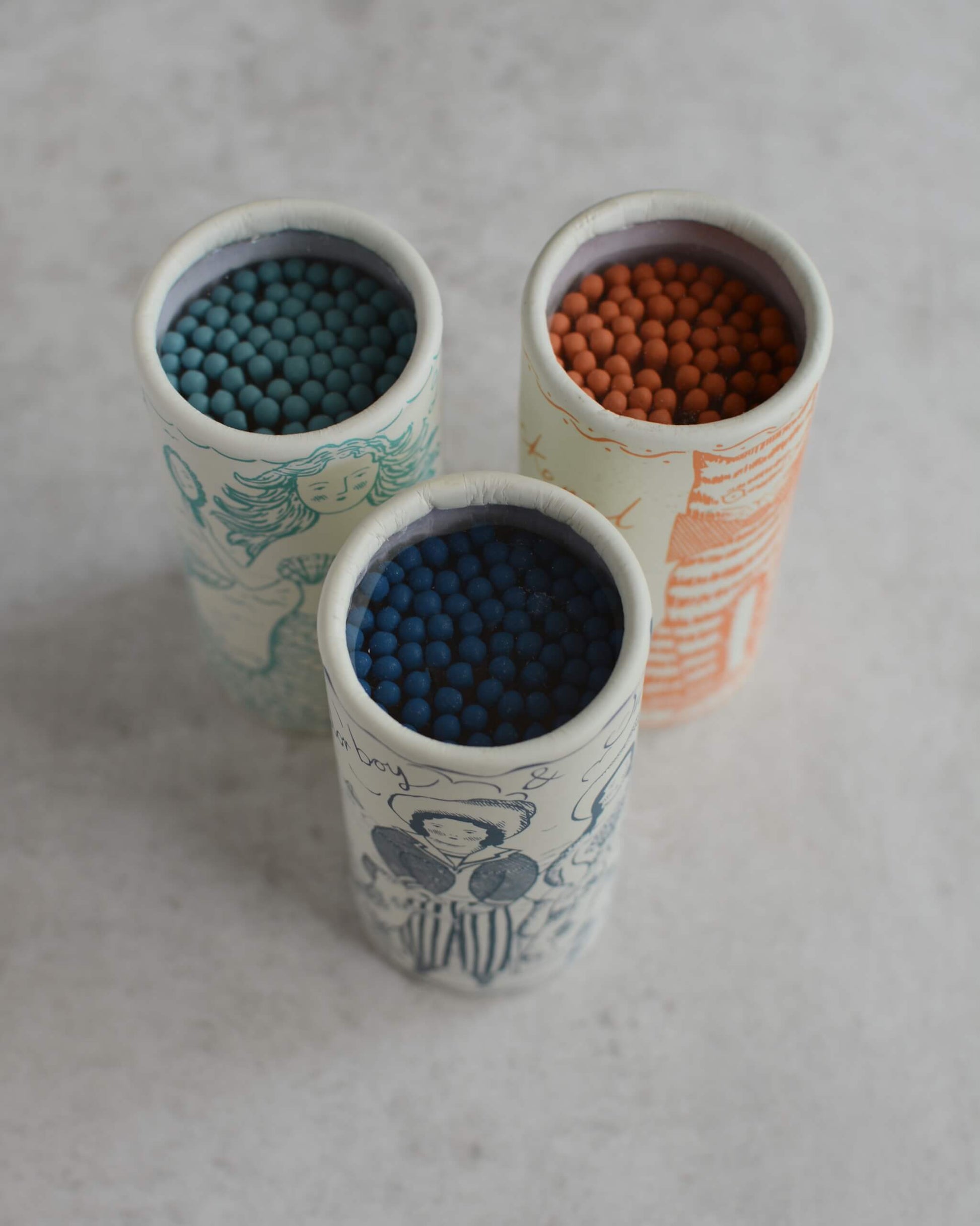 Three cylindrical illustrated match tubes from above, showing the colourful match tips.
