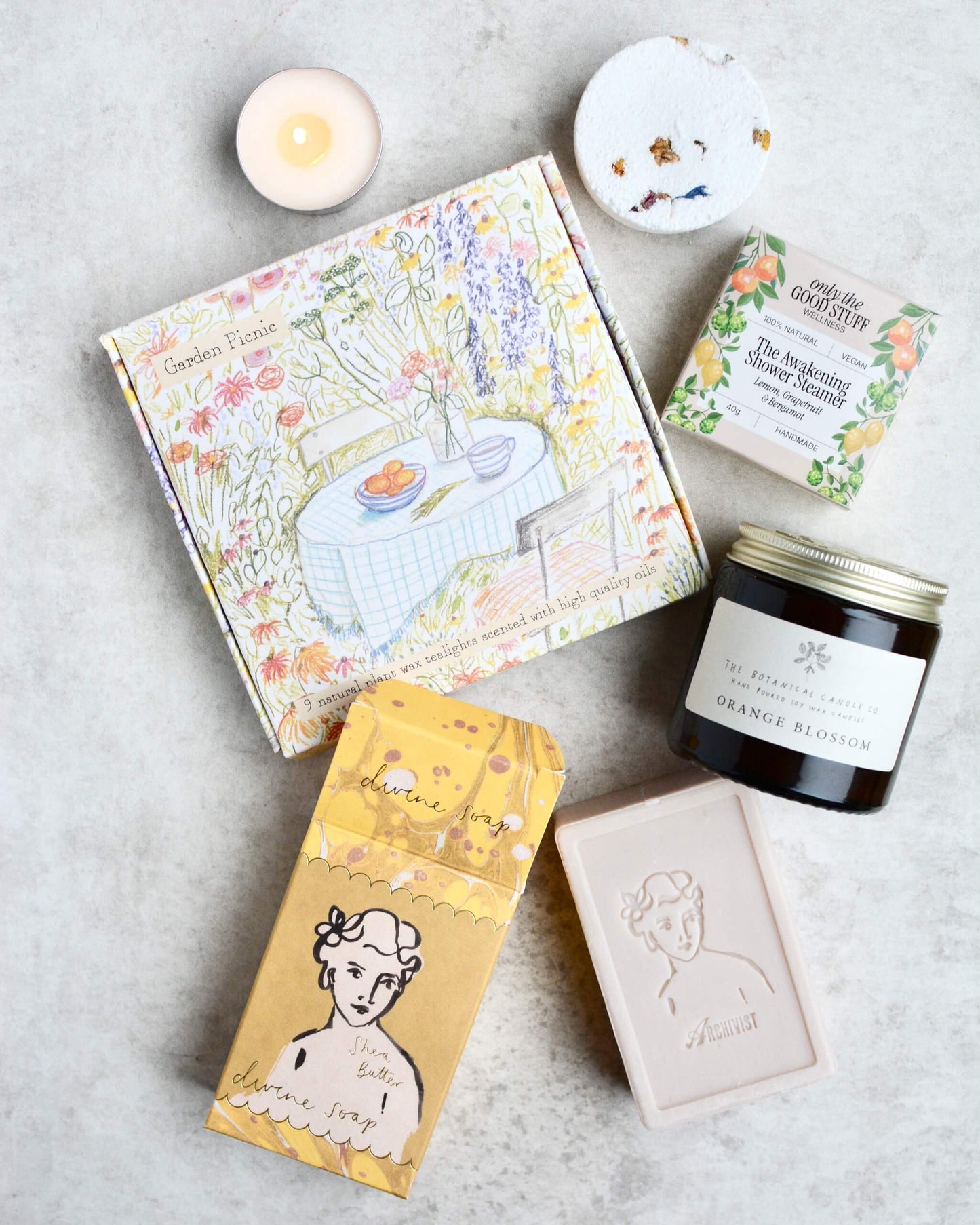 Collection of self care products including a soap, candles, and a shower steamer on a neutral background.