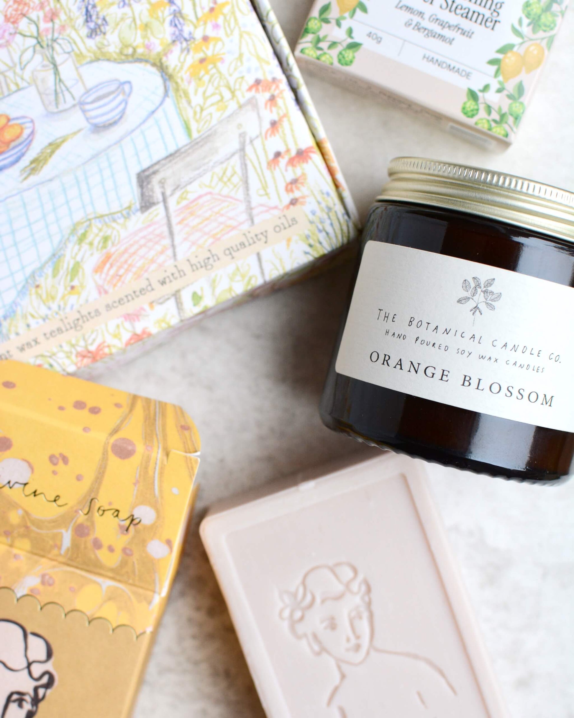 Collection of soap, candle, and shower steamer with decorative boxes on a light surface.