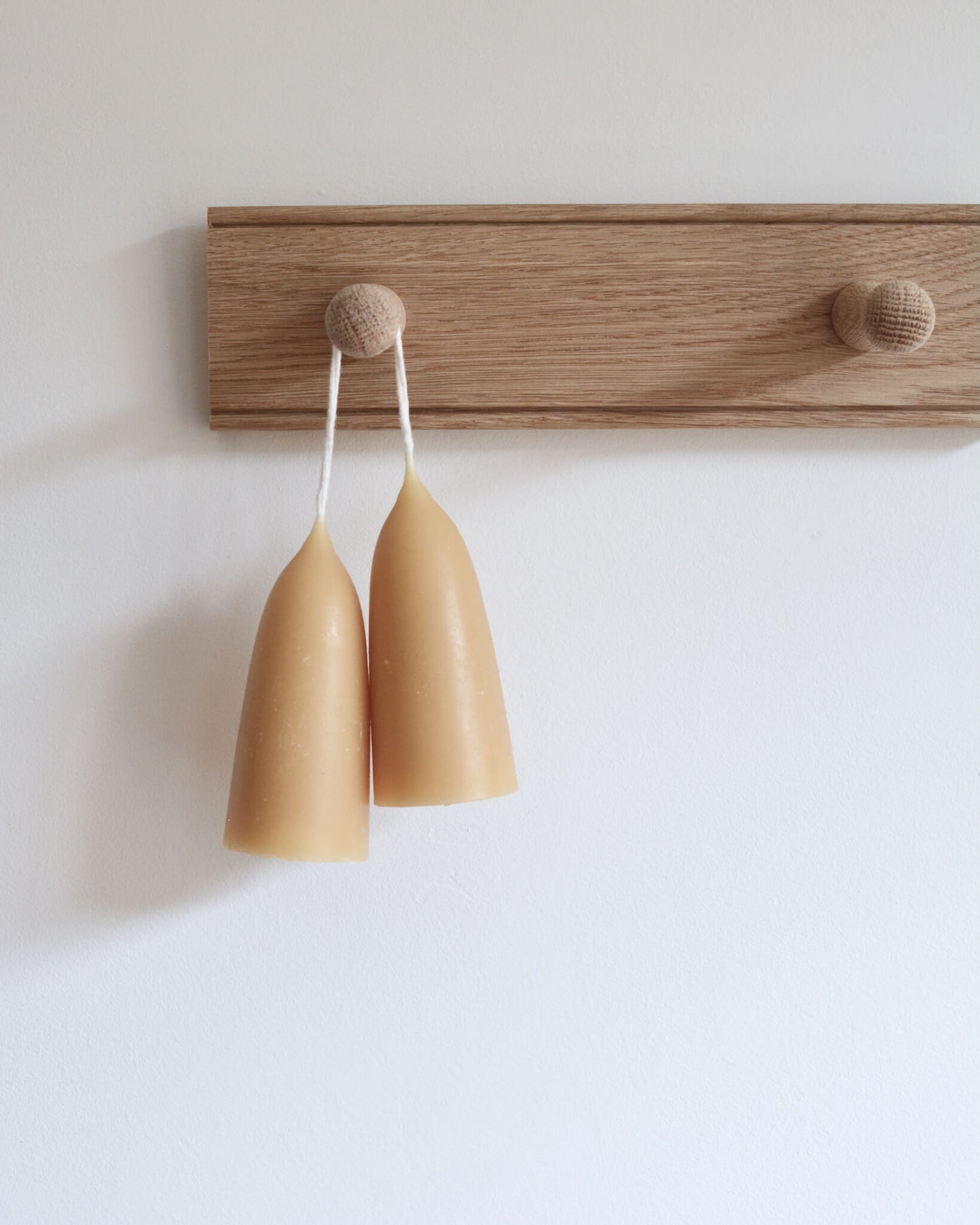 An oak peg rail with 2 pegs by Creamore Mill and a pair of stubby beeswax candles