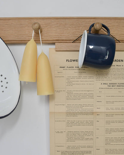 Oak peg rail with stubby beeswax candles and kitchen enamelware.