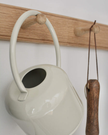 Cream enamel watering can and garden tool, hanging on an oak peg rail.