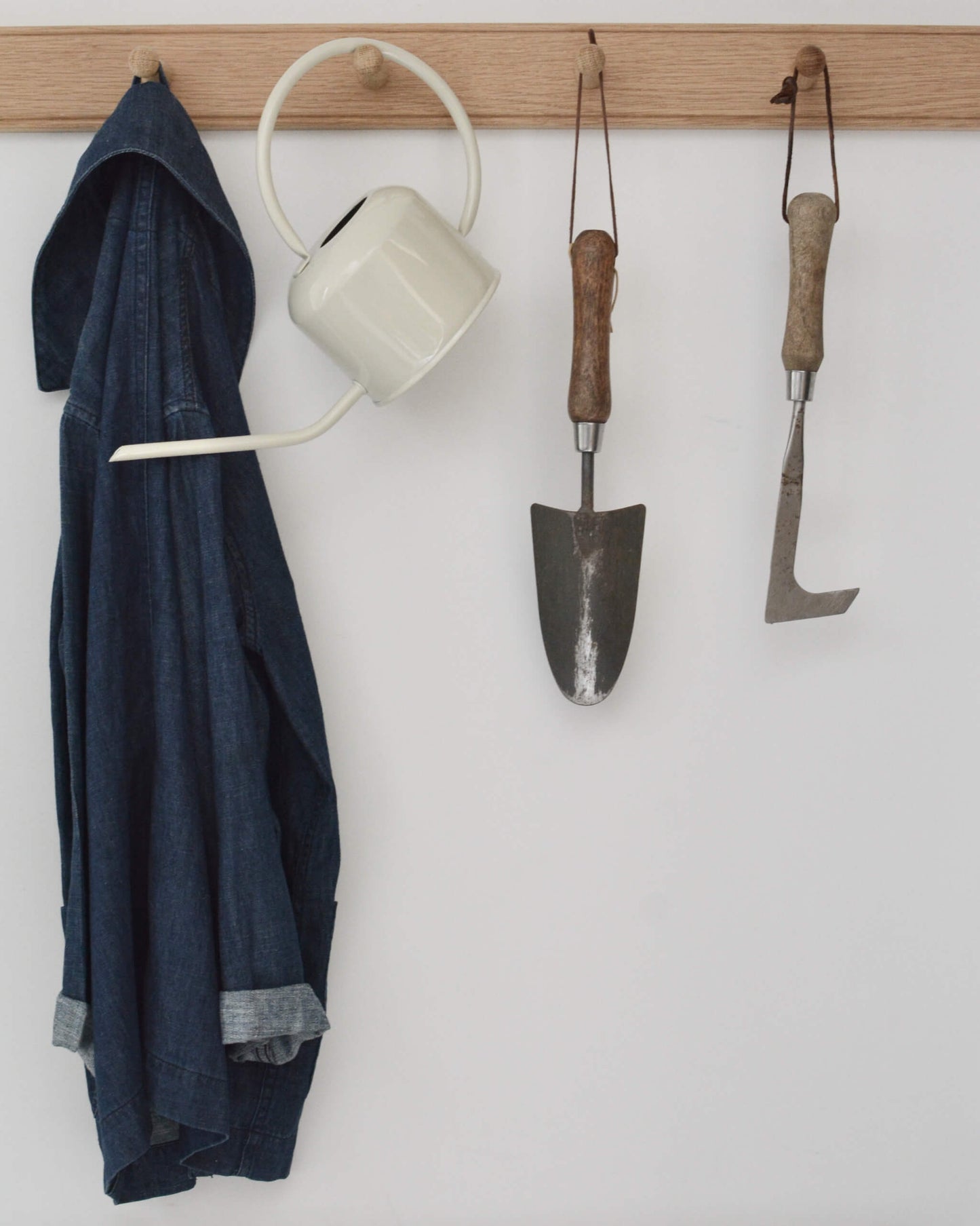 An oak shaker peg rail with a jacket, watering can, and gardening tools hanging from the pegs