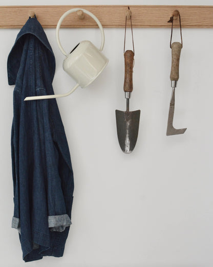 An oak shaker peg rail with a jacket, watering can, and gardening tools hanging from the pegs