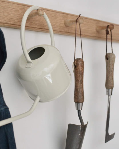 Close-up of an oak shaker peg rail with a watering can, and gardening tools hanging from the pegs