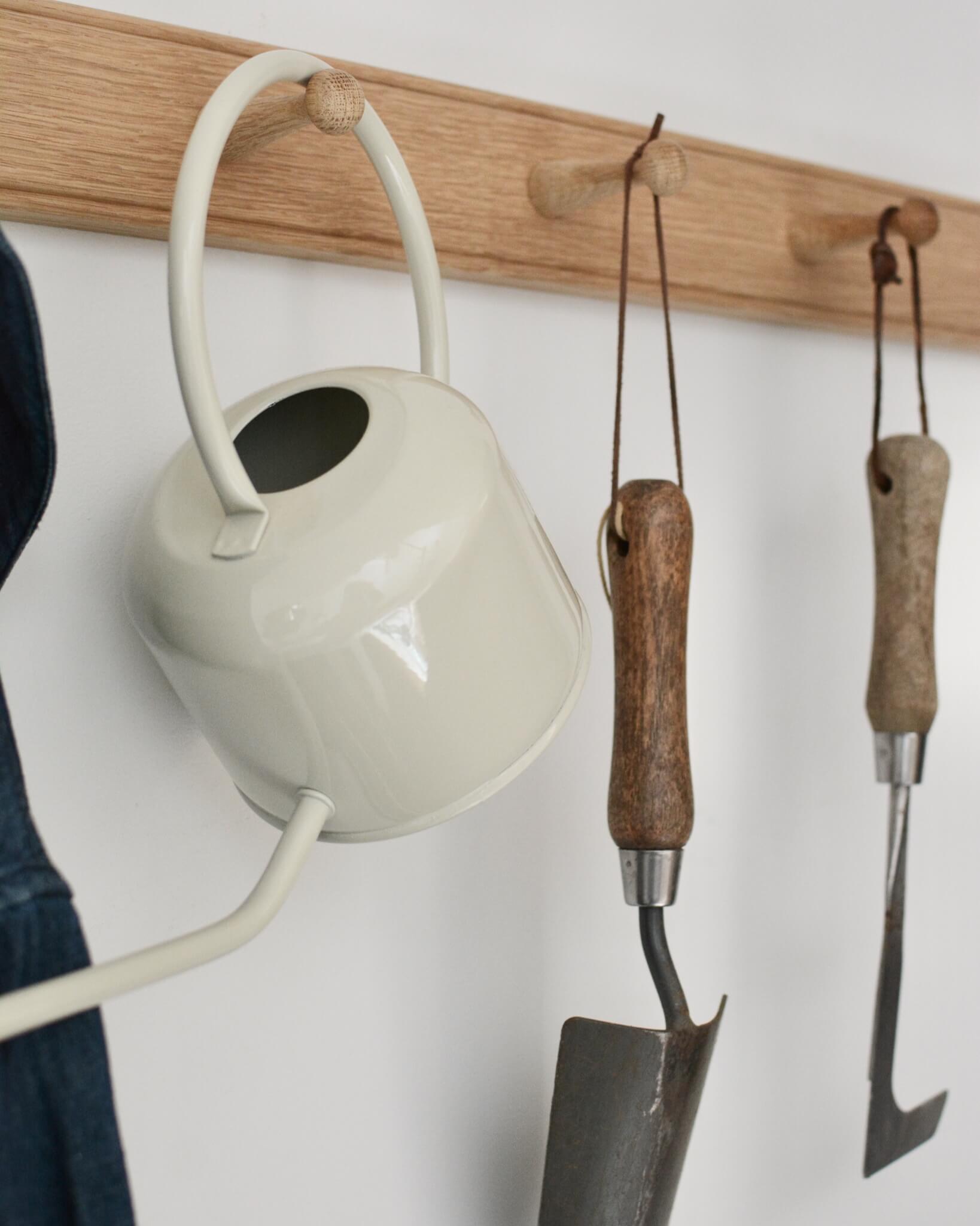 Close-up of an oak shaker peg rail with a watering can, and gardening tools hanging from the pegs