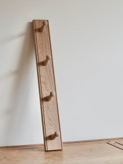 Wooden shaker coat rack with four hooks against a white wall.