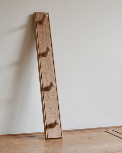 Wooden shaker coat rack with four hooks against a white wall.