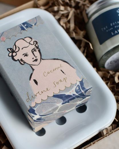 Bar of soap with a decorative packaging and a soap dish, within a gift box.