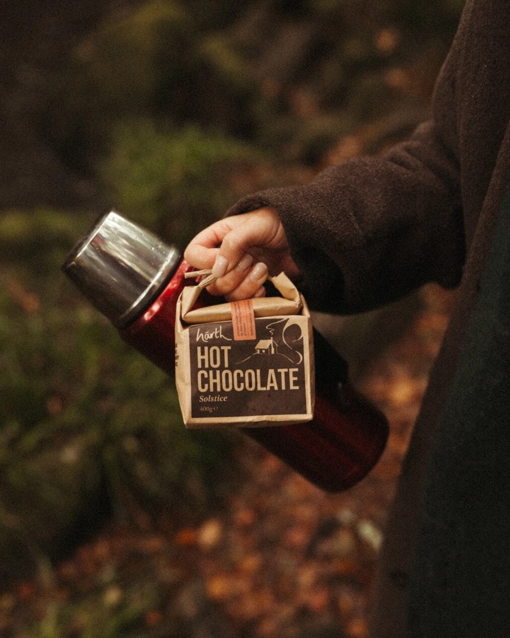 Hand holding a small box of hot chocolate with a forest background