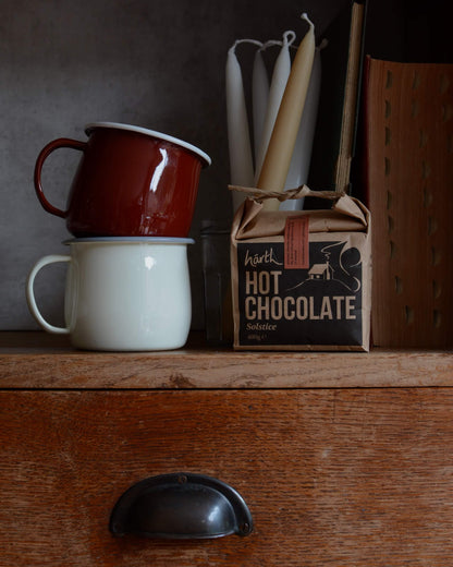 Two mugs stacked on a wooden surface with a box of hot chocolate in the background.