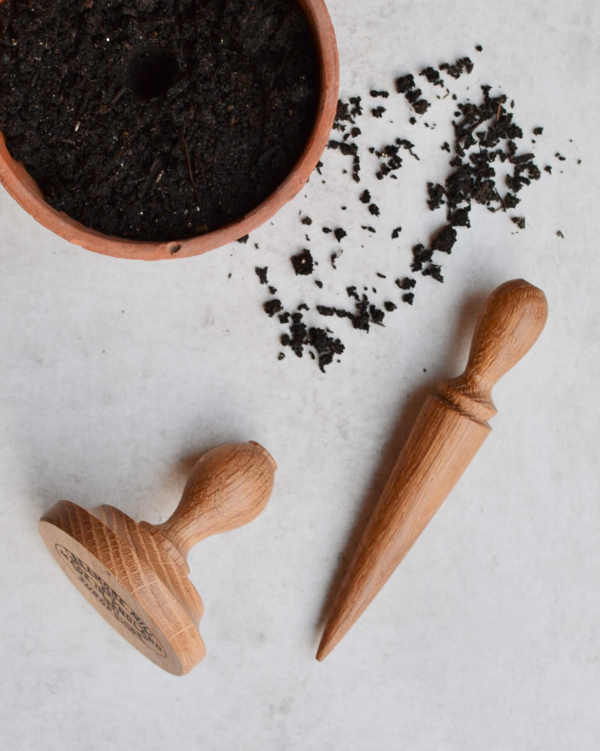 Wooden gardening tools and a small container of soil on a light surface