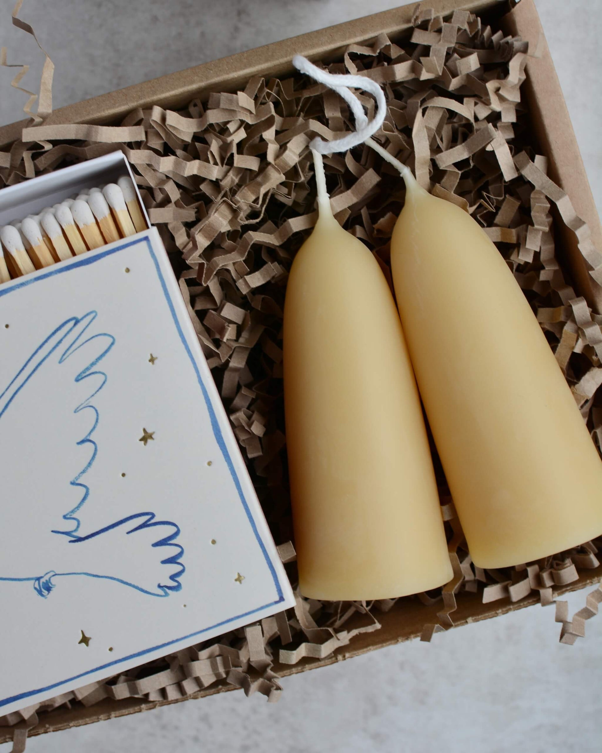 A pair of stubby beeswax candles and a box of matches, shown in a gift box.