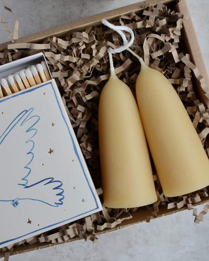 A pair of stubby beeswax candles and a box of matches, shown in a gift box.